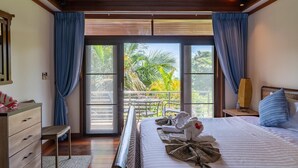 Ein Schlafzimmer mit einem großen Bett, einer Holzkommode, einem Nachttisch und Blick auf einen Balkon mit Pflanzen.