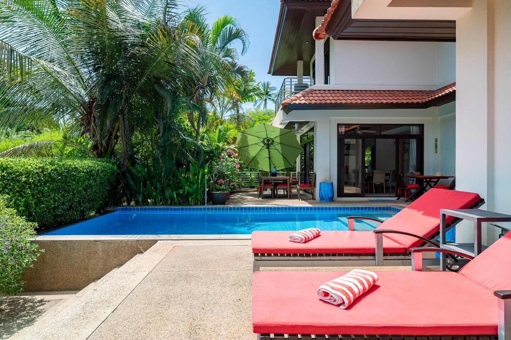 A pool area with red lounge chairs, a small table, and a covered seating area.