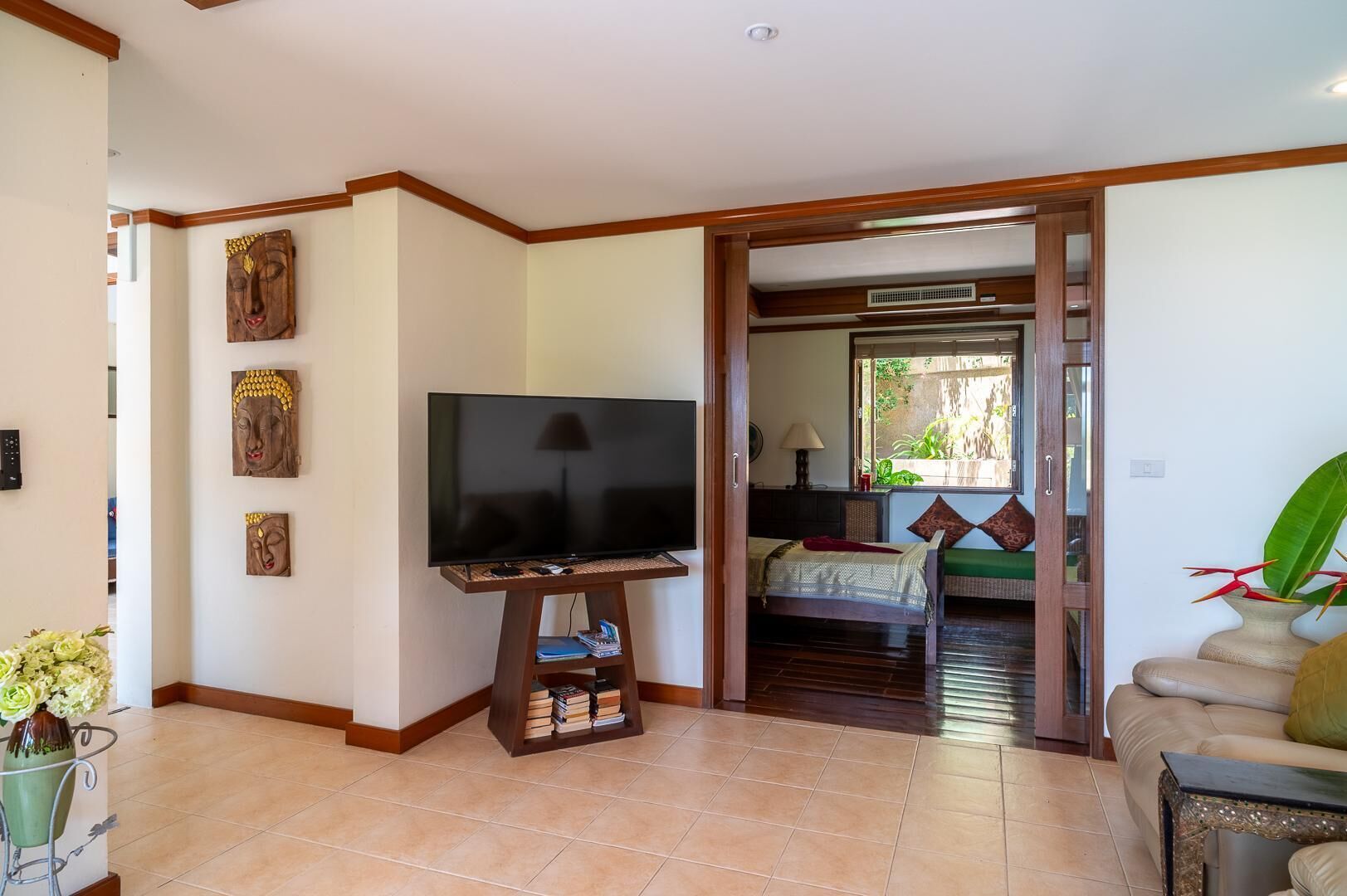 A living room with a television on a wooden stand, a bookshelf, a sofa, and a dining area with a table and chairs.