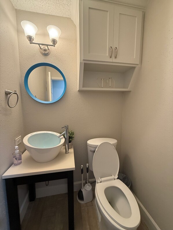 A bathroom with a white sink, a round mirror, a toilet, and a cabinet above the toilet. - Welcome to Sweet Escape Sugar Land, your cozy home away from home! Close to NRG (Sugar Land)
