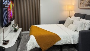 Een moderne hotelkamer met een bed, een aan de muur bevestigde televisie, een nachtkastje en een lamp.