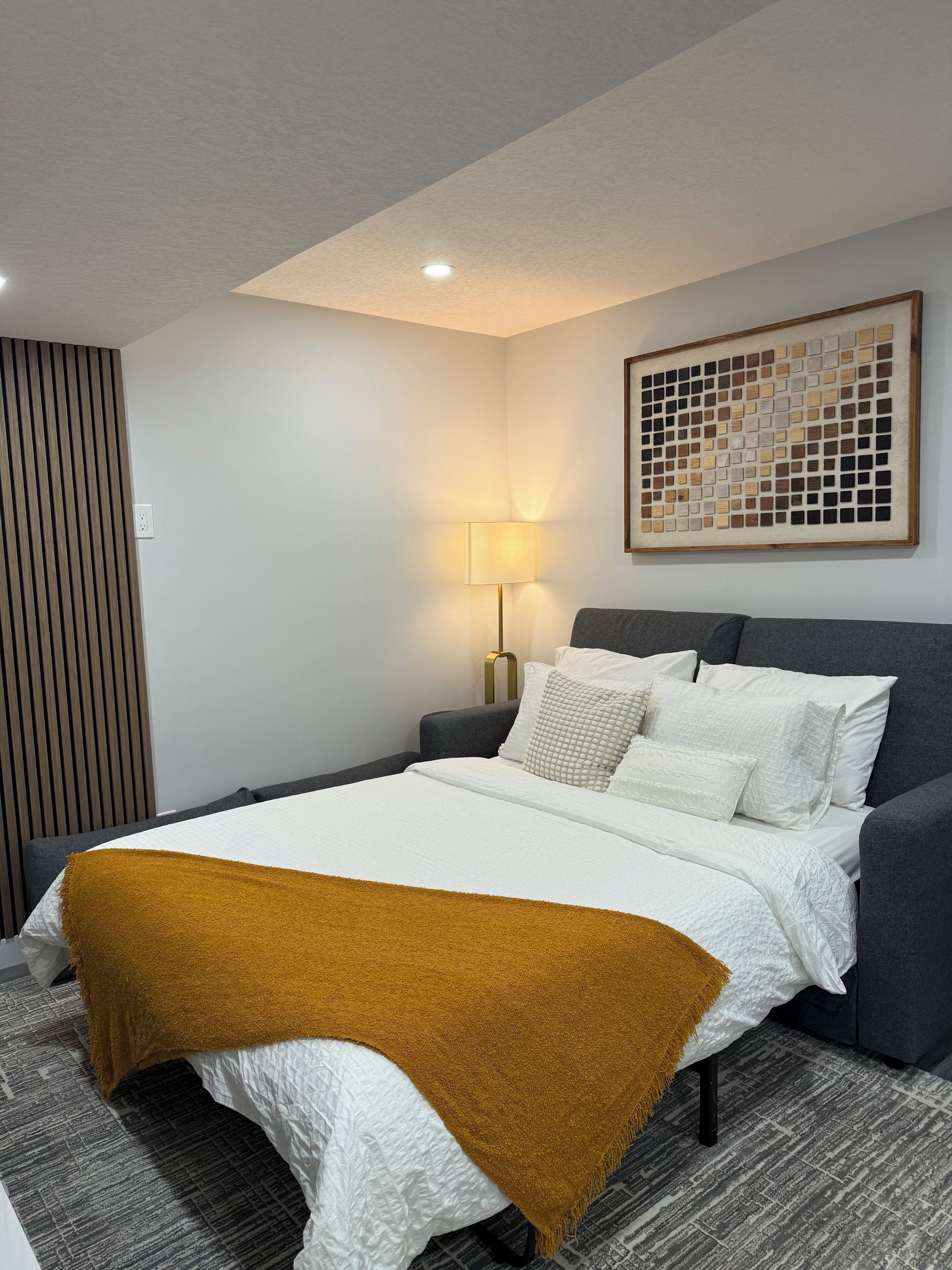 A modern hotel room with a neatly made bed, a bedside lamp, and a decorative wall piece.