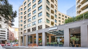 Ein modernes Hotel mit geschwungener Fassade, großen Fenstern und einem überdachten Eingangsbereich mit Pflanzen.