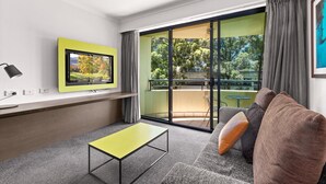 Ein modernes Wohnzimmer mit einer Couch, einem kleinen Tisch, einem Fernseher und einem Balkon mit Blick auf Bäume.