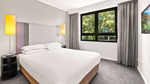 Ein modernes Hotelzimmer mit einem großen Bett, zwei Nachttischlampen, einem Fenster mit Vorhängen und einem Flachbildfernseher an der Wand.