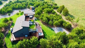 Ett modernt hus med en stor terrass, omgivet av tät grönska och en välskött gräsmatta.