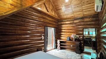 L’intérieur d’une cabane en rondins, avec un lit, des murs en bois, un luminaire au plafond et une fenêtre.