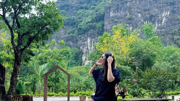 Eine Person sitzt auf einem hölzernen Stuhl in einem Garten mit Blick auf eine gebirgige Landschaft.