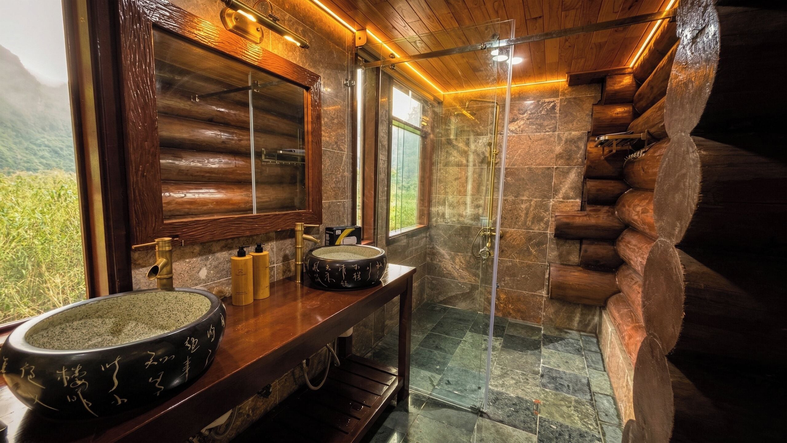 A bathroom with a large basin, a mirror, and a shower area with a stone wall.