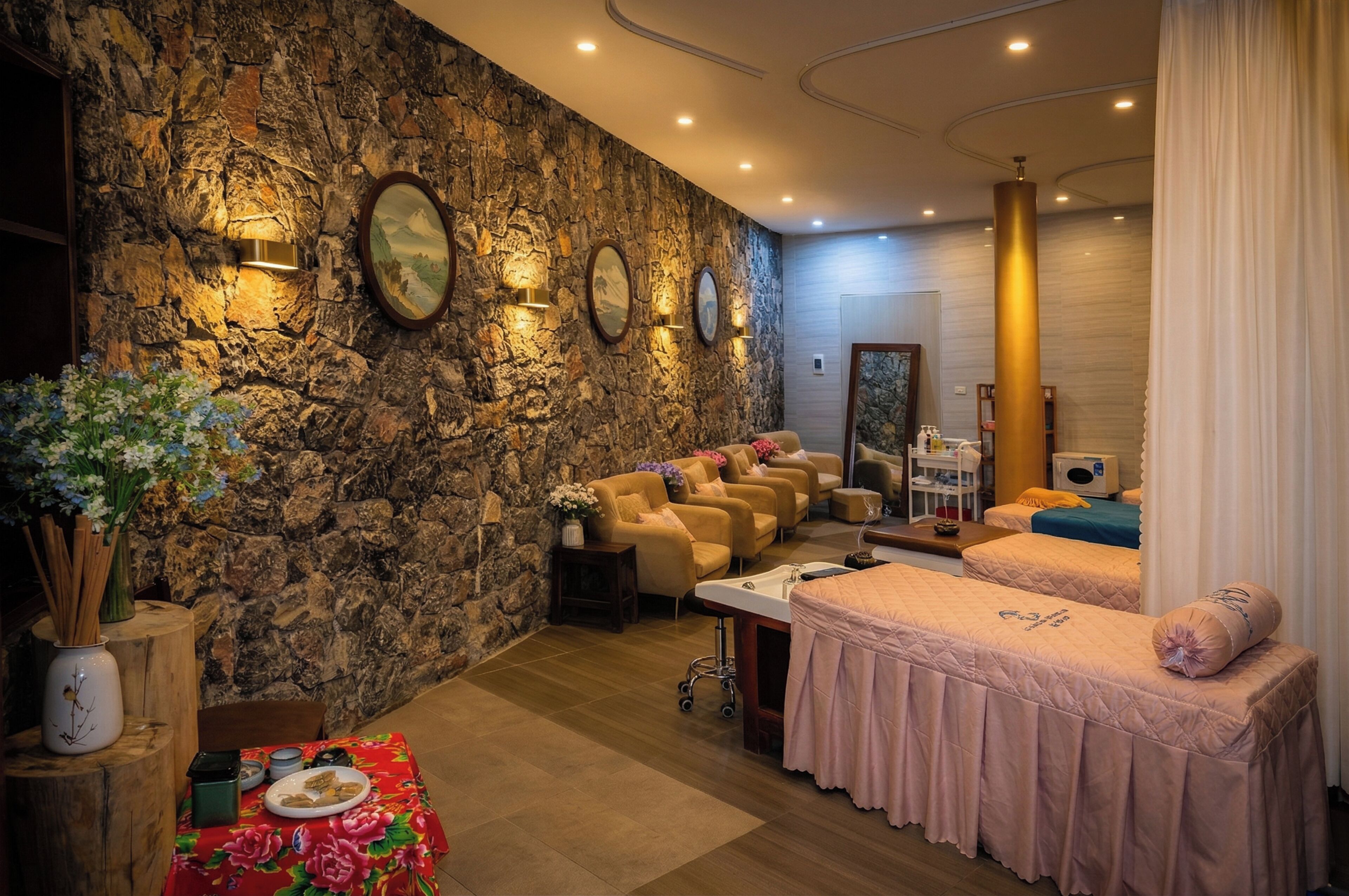 Un salón de spa con pared de piedra, sillas de masaje, camilla de tratamiento y una zona de recepción.