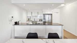 A modern kitchen with white cabinets, a stainless steel refrigerator, and a marble countertop. - Ocean View 3-bed With Gym, Pool (Gold Coast)