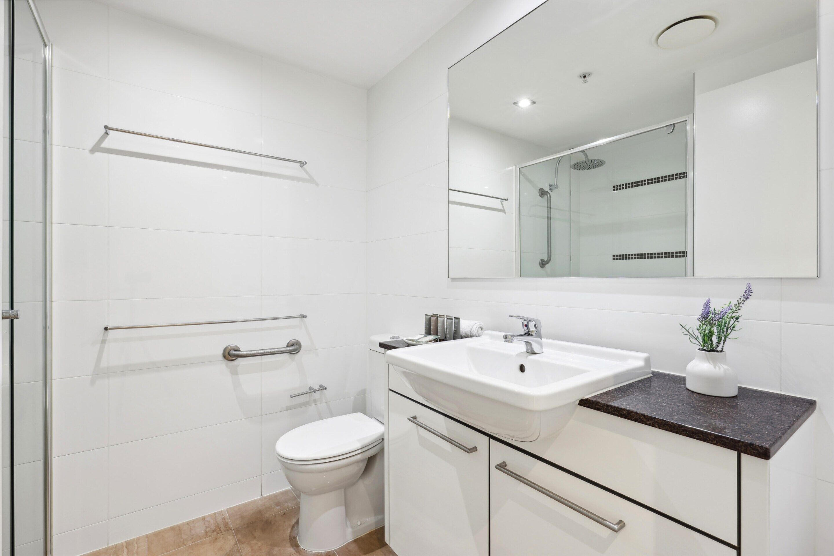 A modern bathroom with a white toilet, a glass shower enclosure, a white sink with a marble countertop, and a mirror above the sink.