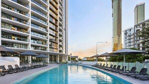 A swimming pool with lounge chairs and umbrellas, surrounded by high-rise buildings. - Ocean View 3-bed With Gym, Pool (Gold Coast)