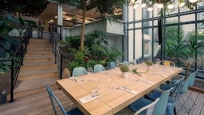 Eine Holzterrasse mit einem langen Esstisch, umgeben von Stühlen, und einer Treppe zu einer erhöhten Ebene.