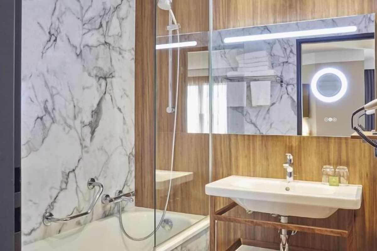 Une salle de bain avec un mur en marbre, un meuble-lavabo en bois, un lavabo et une douche.