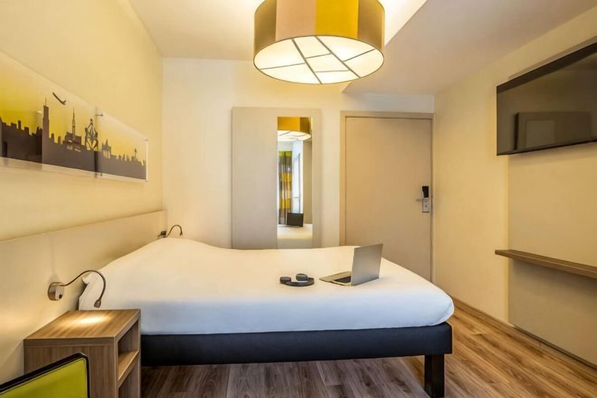 Hotelkamer met een bed, een bureau, een stoel, een televisie en een stadsgezicht schilderij aan de muur.