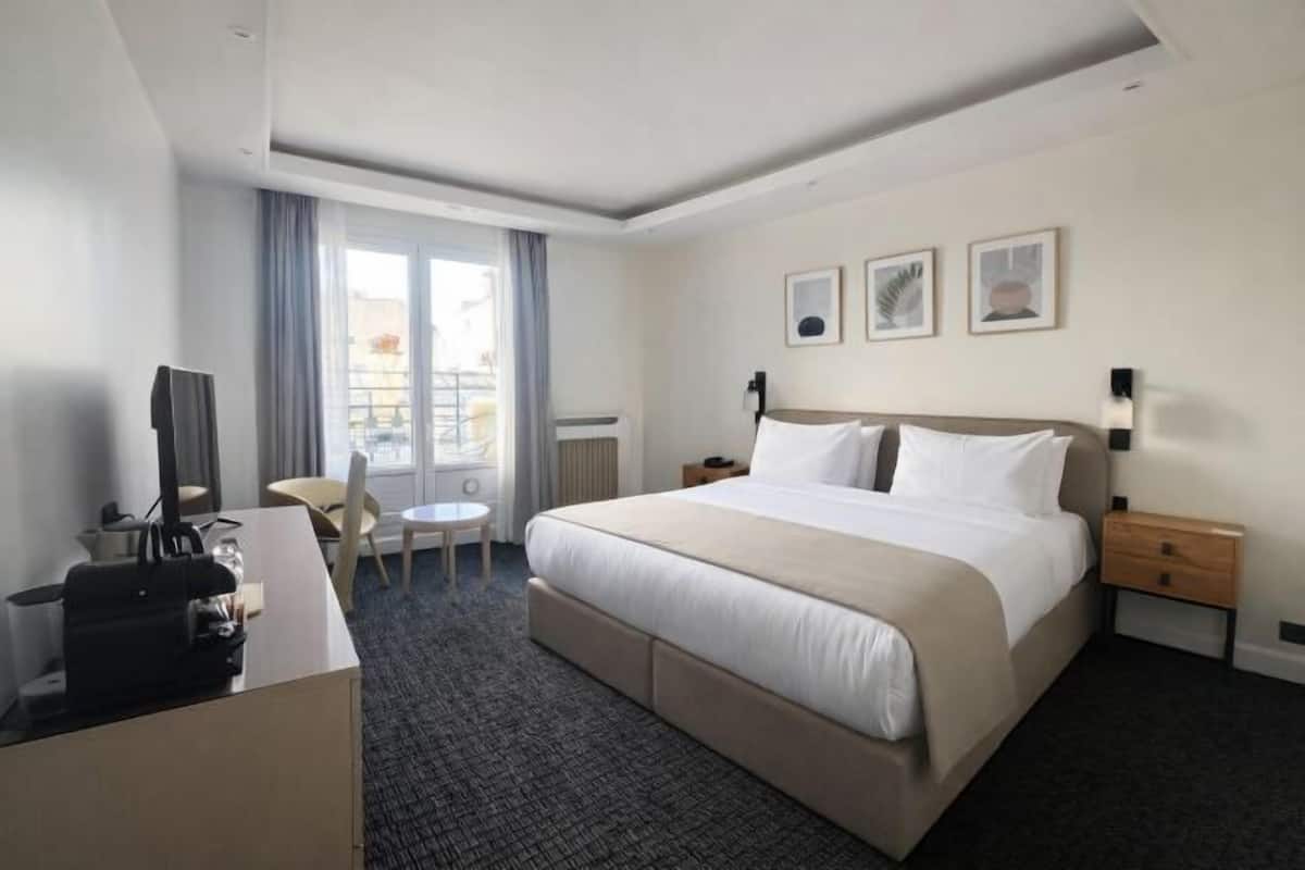 Ett hotellrum med en säng, ett skrivbord, en stol, en tv och ett fönster.