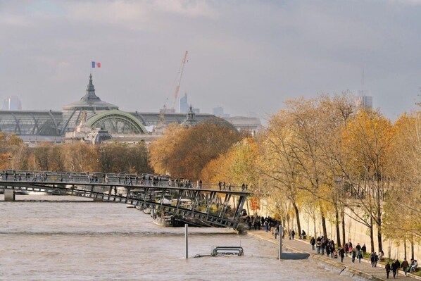 A bridge over a river with a view of a large building with a dome and a flag in the background.