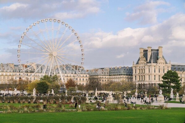 Una noria grande, un parque con estatuas y edificios históricos.