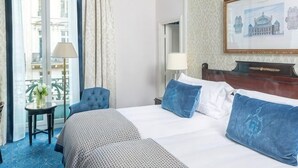 Una habitación de hotel con cama, una silla, una mesa, una lámpara y un cuadro en la pared.