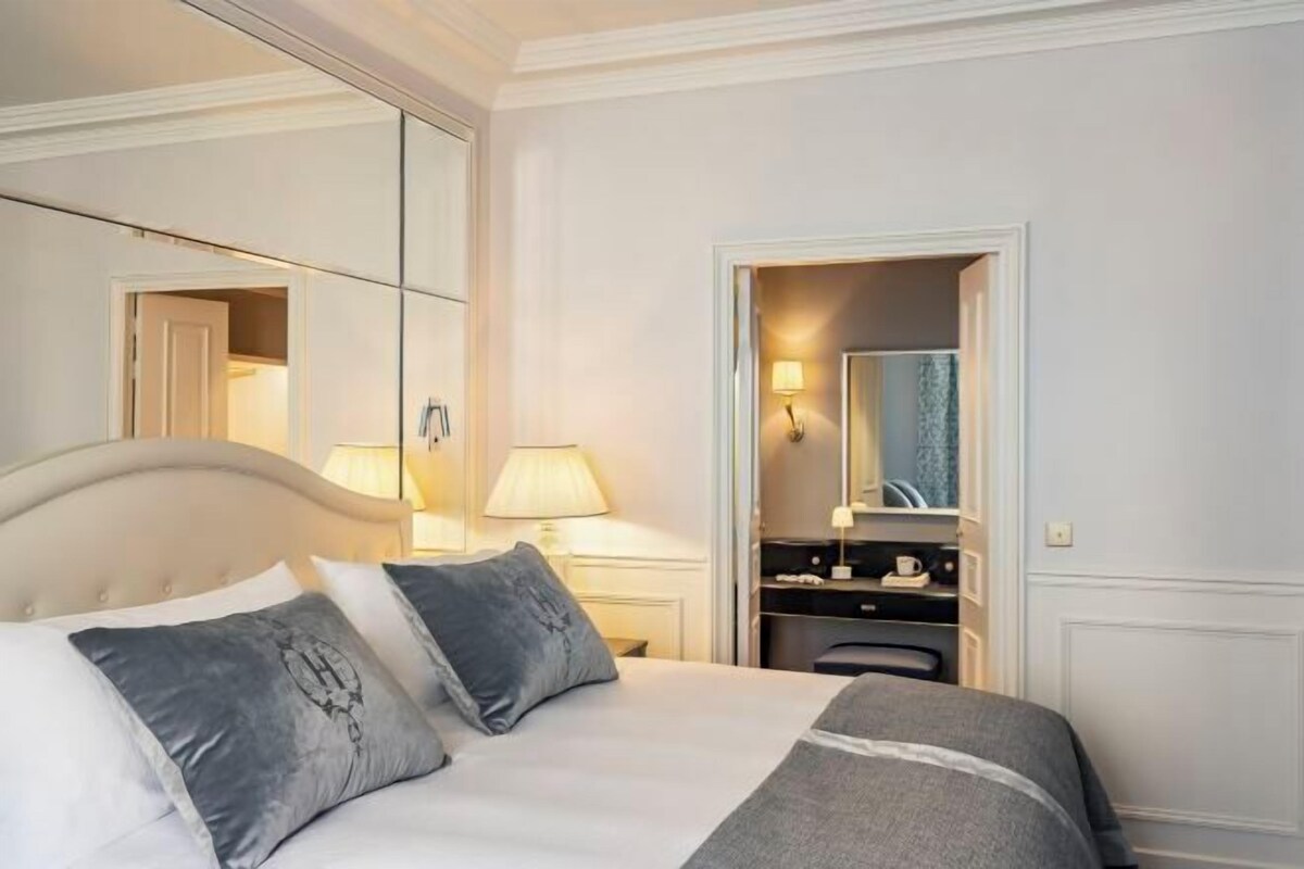 Una habitación de hotel con cama, lámparas de noche, un espejo, escritorio y armario.