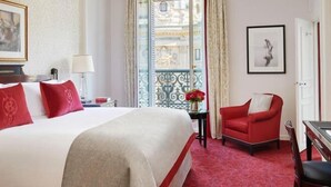 Habitación de hotel con una cama grande, un sillón rojo, una mesita con una lámpara y vistas a través de un ventanal.