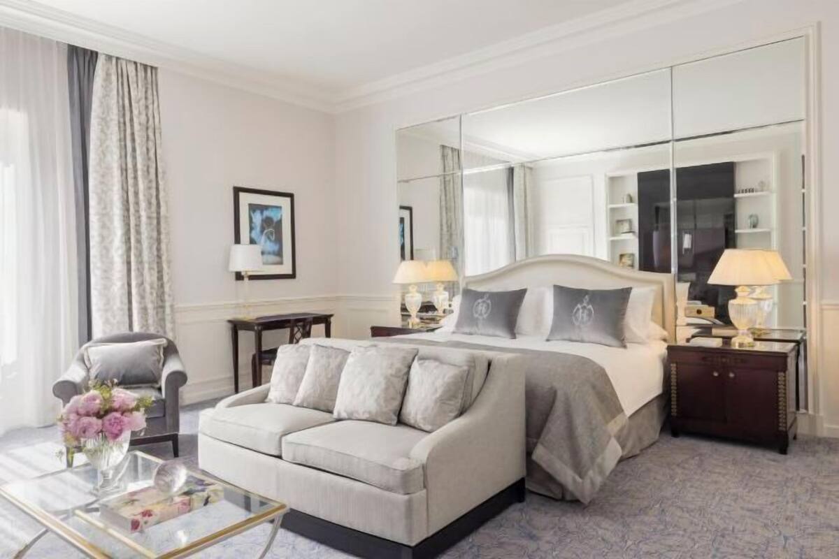 A hotel room with a bed, a sofa, a mirror, and a side table.