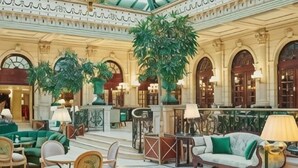 Un lobby espacioso con suelos de mármol, sofás verdes y grandes macetas con plantas.