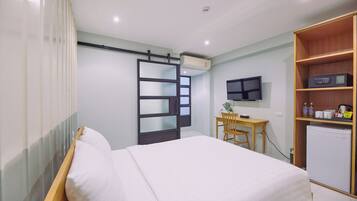 Una habitación de hotel con cama, escritorio, televisor y un refrigerador pequeño.