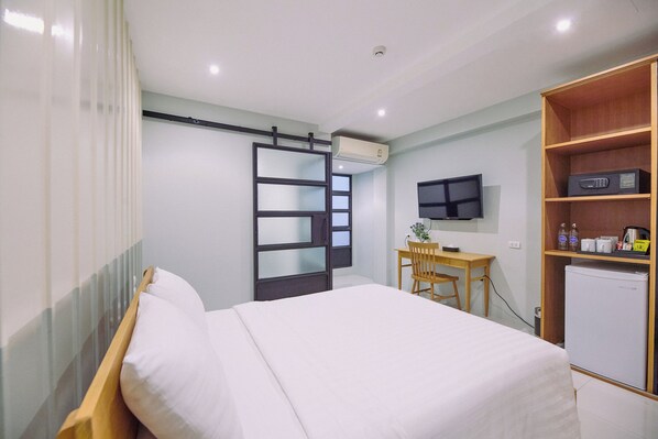 A hotel room with a bed, a desk, a television, and a mini-fridge. - Go2bed Pattaya (Pattaya)