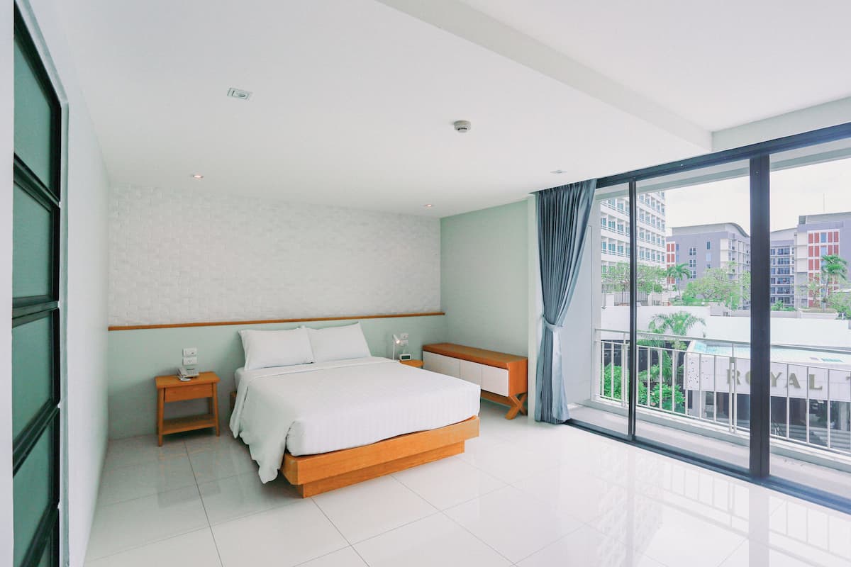 Quarto de hotel moderno com uma cama grande, uma mesinha de cabeceira e vista da cidade por grandes janelas.