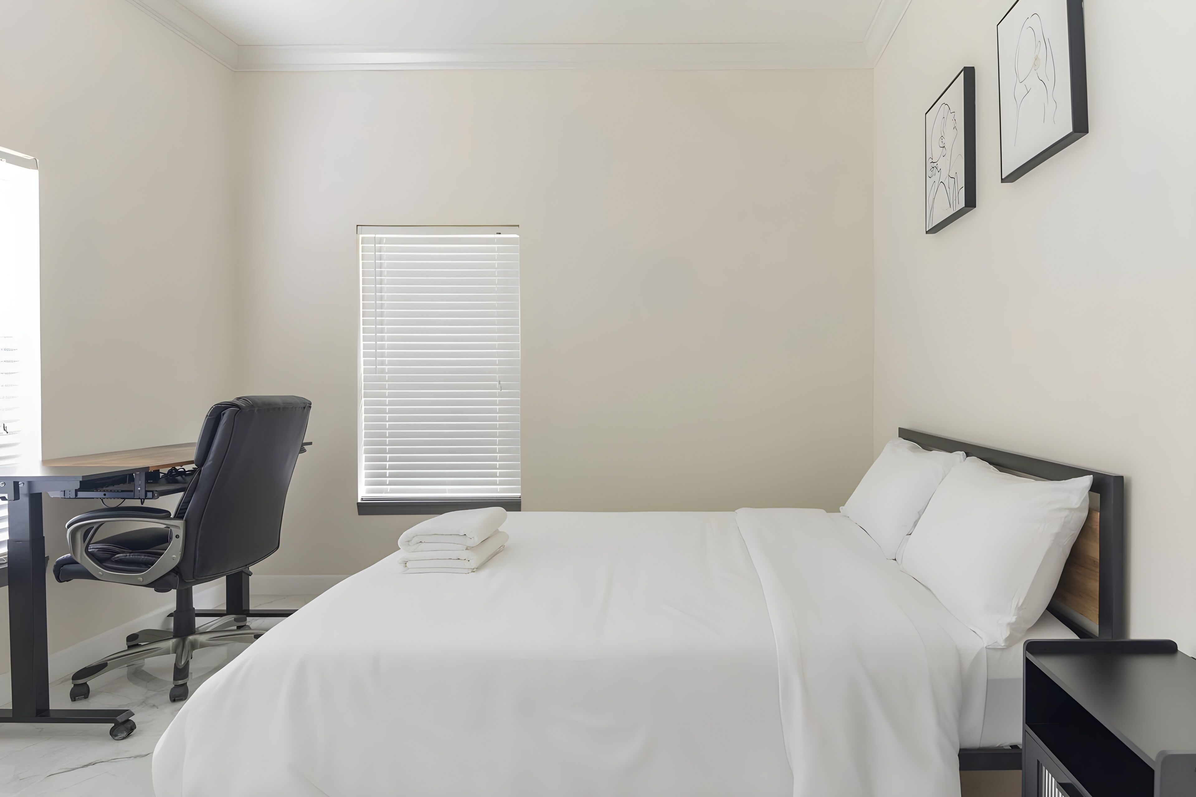 Hotellihuone, jossa on sänky, työpöytä tuolilla ja ikkuna, jossa on sälekaihtimet.