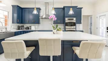 A modern kitchen with dark blue cabinets, a white island with bar stools, stainless steel appliances, and pendant lighting.