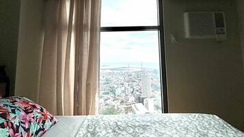 A hotel room with a large bed, a window with curtains, and a view of a cityscape.