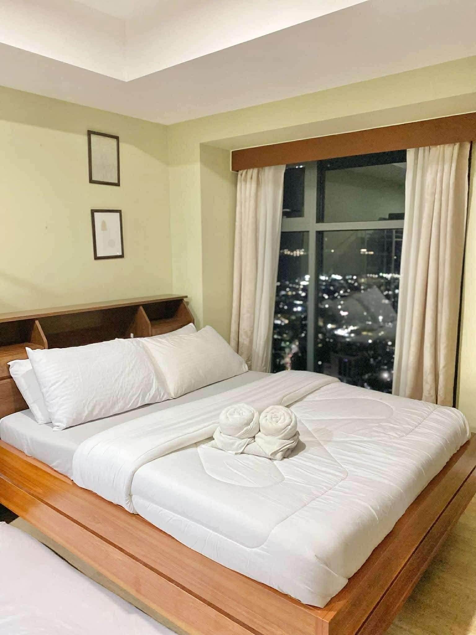 Hotelkamer met een groot bed, houten hoofdeinde en uitzicht op een stadsbeeld in de nacht.
