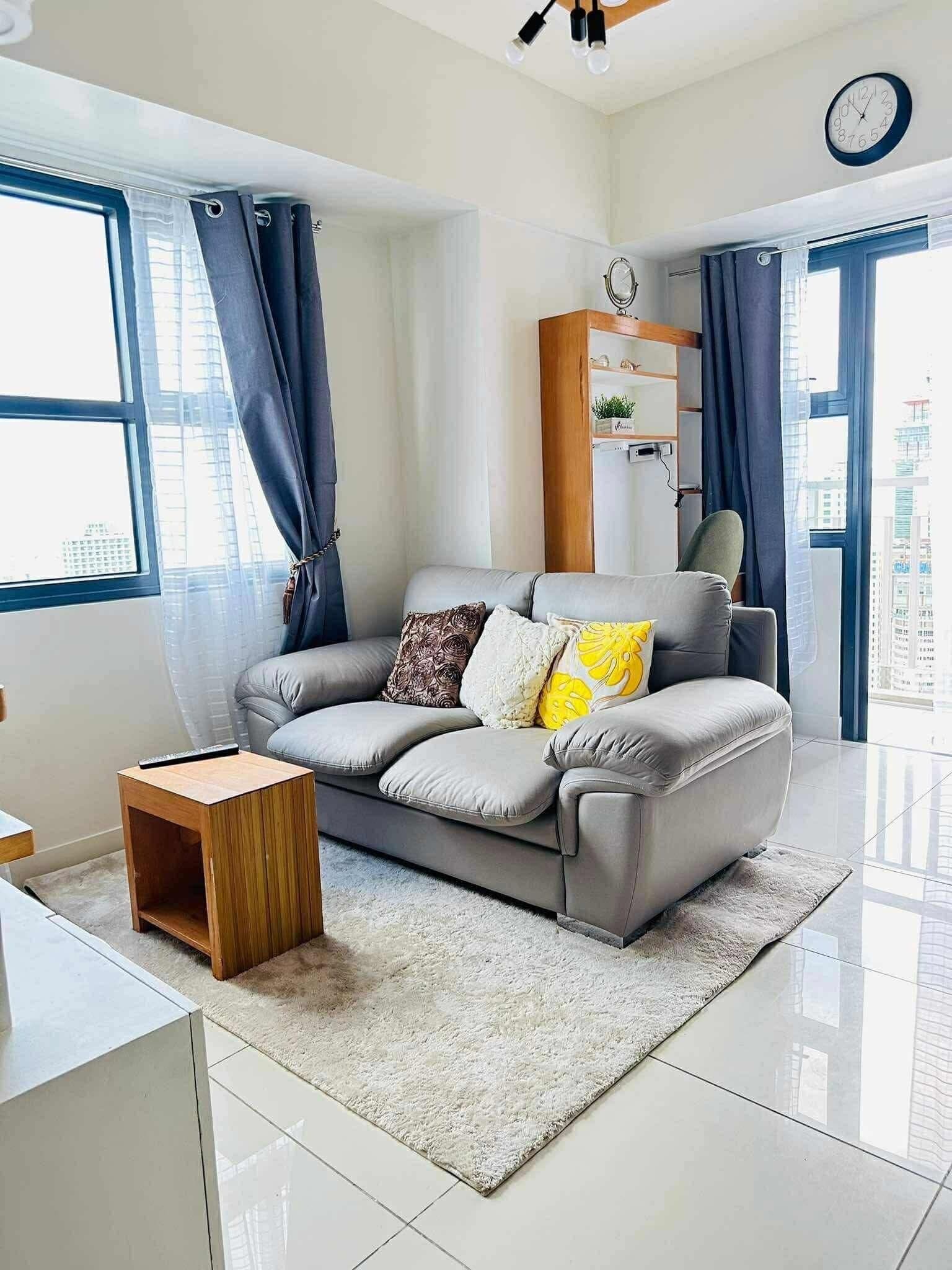 A modern living room with a grey sofa, a small wooden side table, and a white rug.