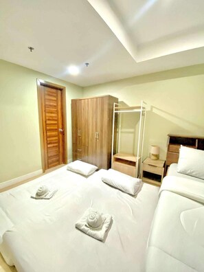 A hotel room with two beds, a wooden wardrobe, a glass shower enclosure, and a bedside table with a lamp. - Horizon 101 Listings (Cebu City)