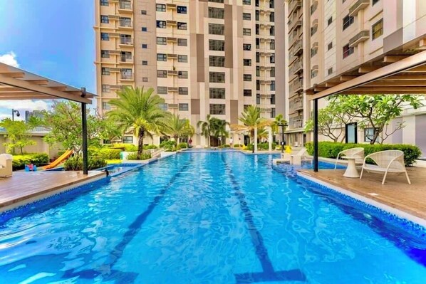 A swimming pool with a clear blue water surface, surrounded by a wooden deck and white lounge chairs. - Horizon 101 Listings (Cebu City)
