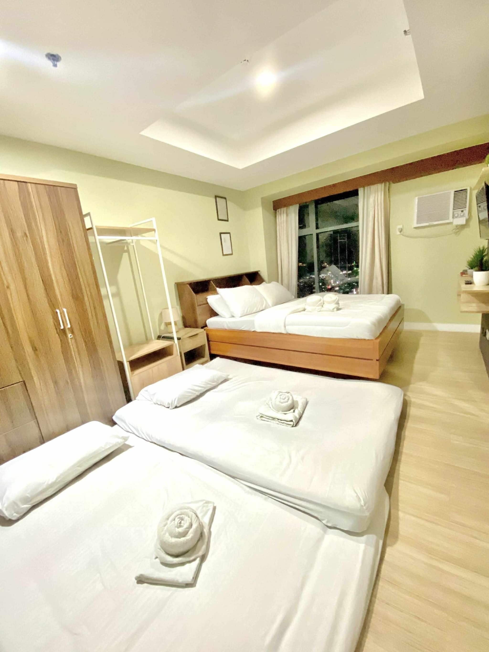 Een hotelkamer met twee bedden, een kledingkast, een raam met gordijnen en uitzicht op de stad 's nachts.
