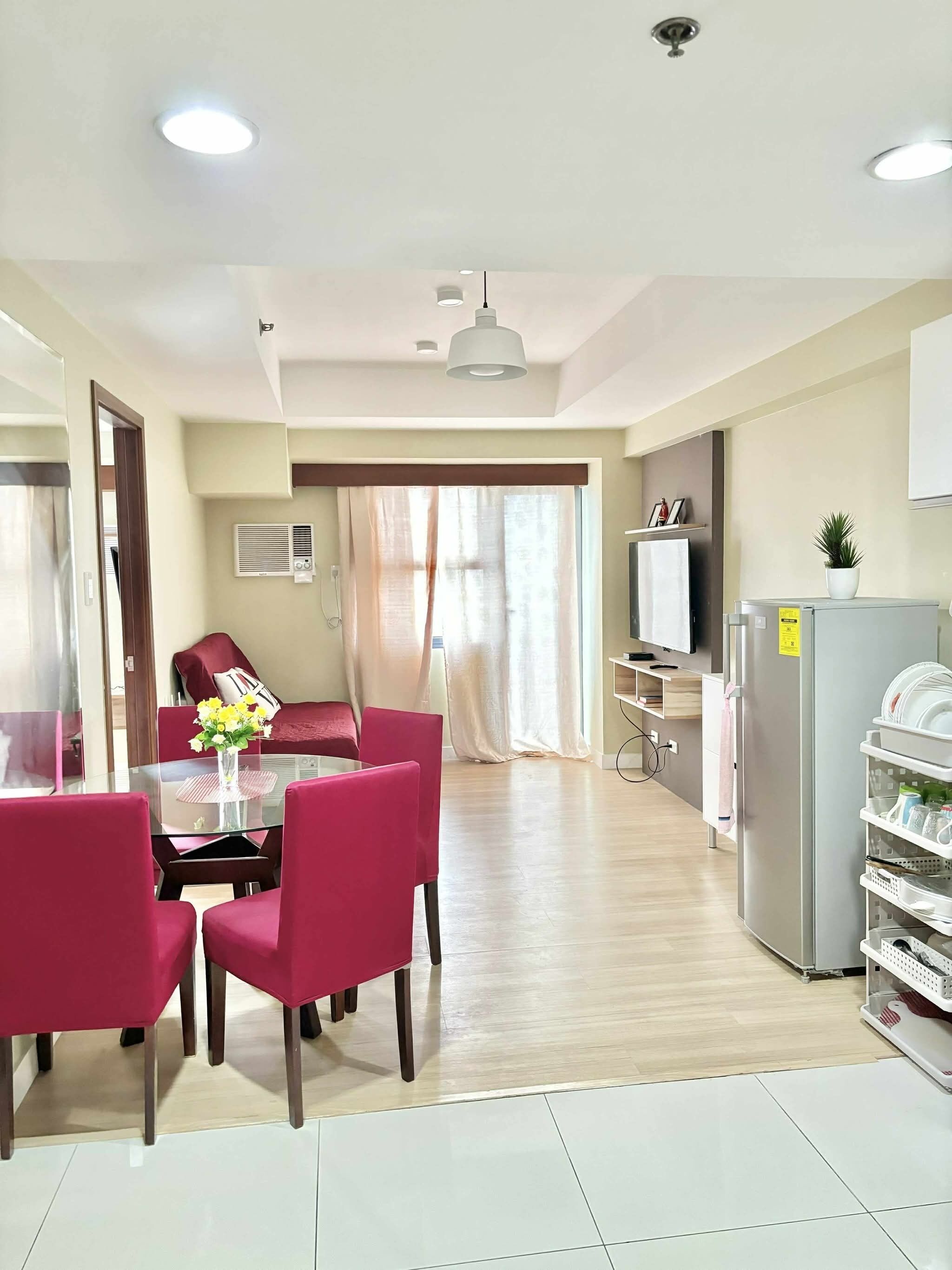 Una cocina moderna con refrigerador, microondas y pileta. Hay un comedor con mesa de vidrio y sillas rojas.