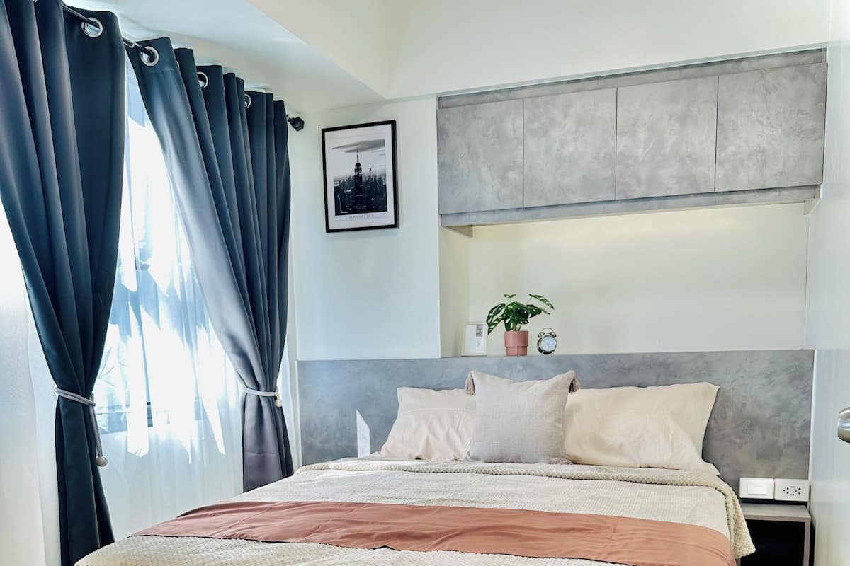 Un dormitorio moderno con una cama grande, una mesita de noche, una estantería en la pared con una planta y un cuadro enmarcado.