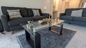 Una sala de estar moderna con dos sofás grises, una mesa de centro de vidrio y objetos decorativos.