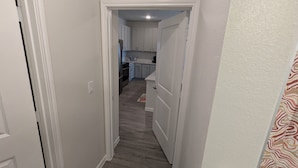 Un pasillo estrecho que conduce a una cocina con armarios blancos y piso de madera.
