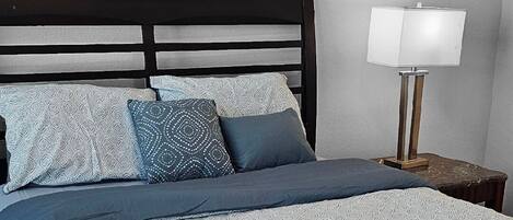 A neatly made bed with a patterned bedspread and pillows, a bedside lamp, and a dark headboard.