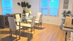 A modern dining area with a glass table, white chairs, and a ceiling fan.