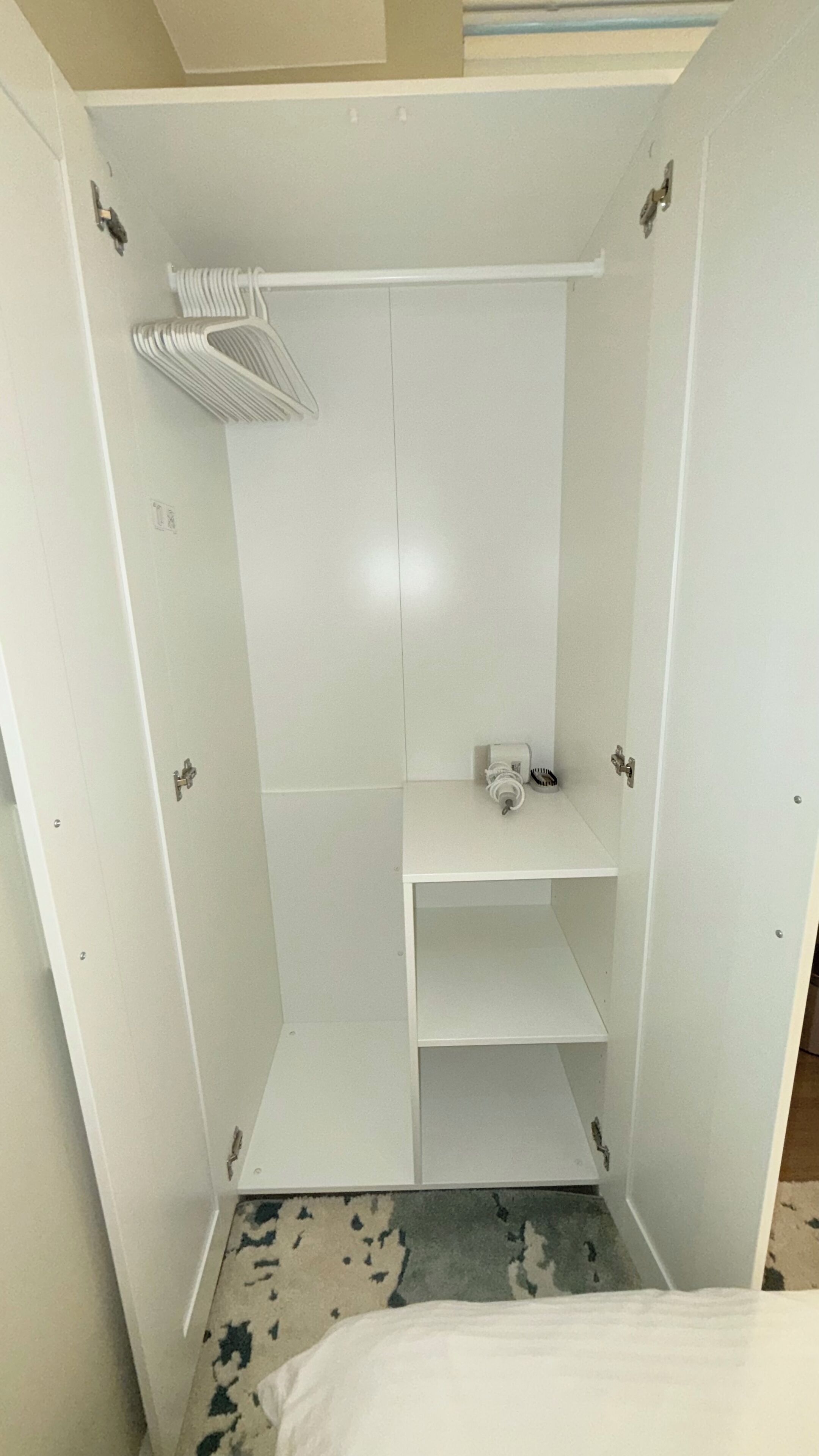Um closet amplo com prateleiras brancas, cabideiro e um pequeno espelho.
