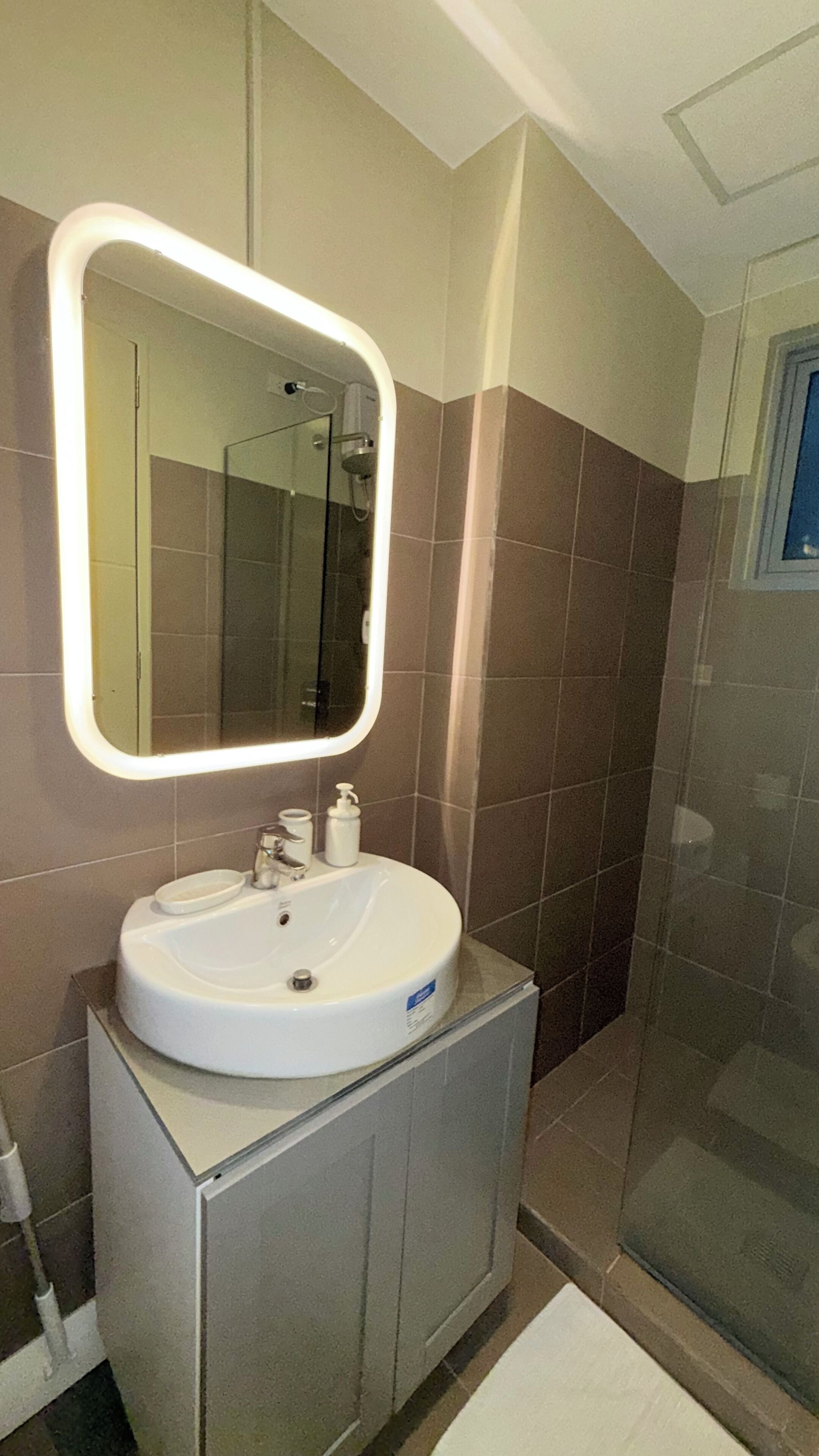 Un baño con lavamanos blanco, un espejo con luz y una ducha.