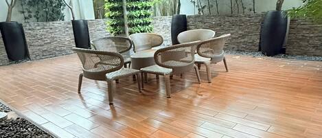 Un patio exterior con suelo de madera, mobiliario de mimbre y una pequeña fuente de agua.