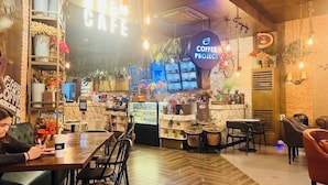 Ein gemütliches Café-Interieur mit einer Kaffeebar, Sitzgelegenheiten und dekorativen Elementen wie Pflanzen und Lampen.