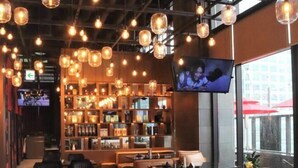 A modern bar area with hanging pendant lights, a television screen, and a seating area with sofas and tables.